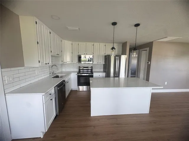 a kitchen with stainless steel appliances granite countertop a refrigerator a stove a sink a chimney a refrigerator and white cabinets with wooden floor