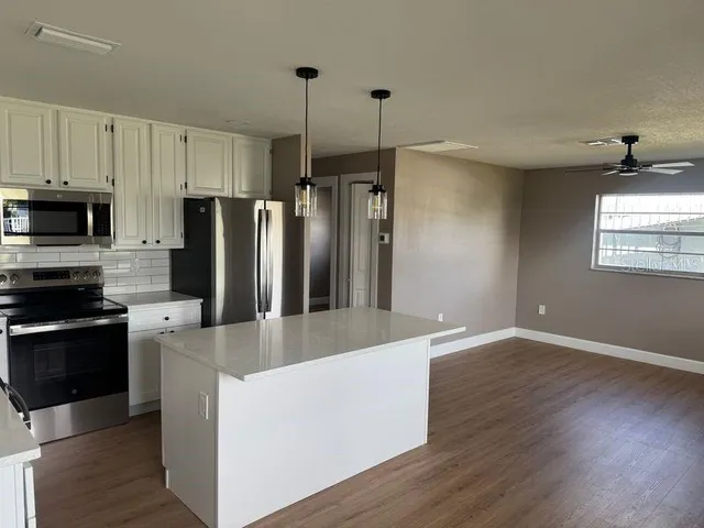 a large kitchen with stainless steel appliances granite countertop a refrigerator a stove a sink and a wooden floor