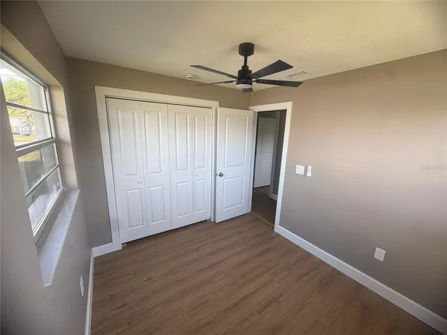 an empty room with wooden floor fan and windows