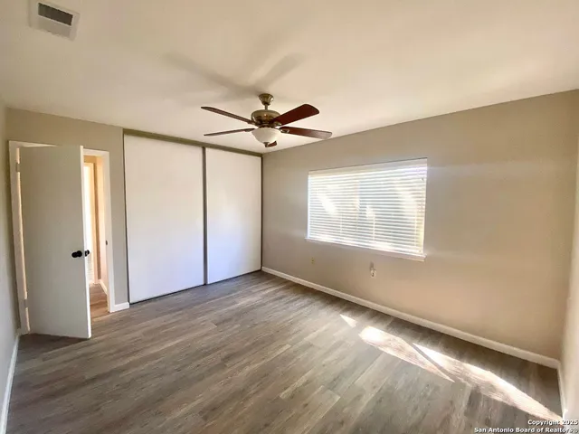 an empty room with wooden floor fan and windows