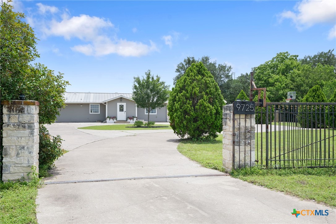 9725 Bock Road Buda, TX 78610 - Photo 2 of 37 A private driveway leads to a welcoming home, framed by mature trees and a robust gate.
