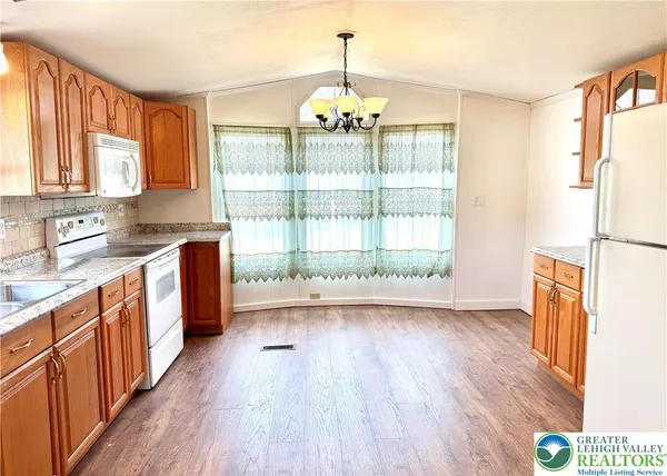 a view of a refrigerator in kitchen and an empty room with wooden floor