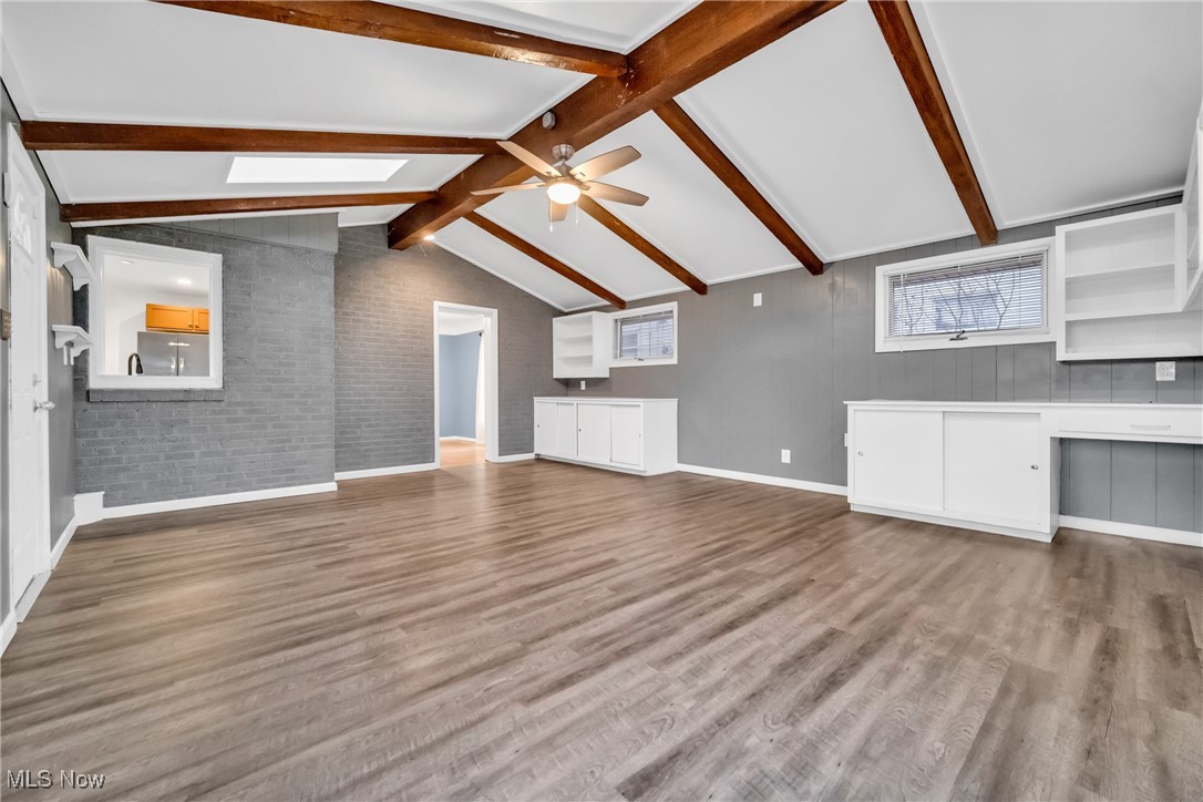 1605 Laclede Road Cleveland, OH 44121 - Photo 21 of 40 Unfurnished living room with baseboards, vaulted ceiling with skylight, brick wall, a ceiling fan, and wood finished floors