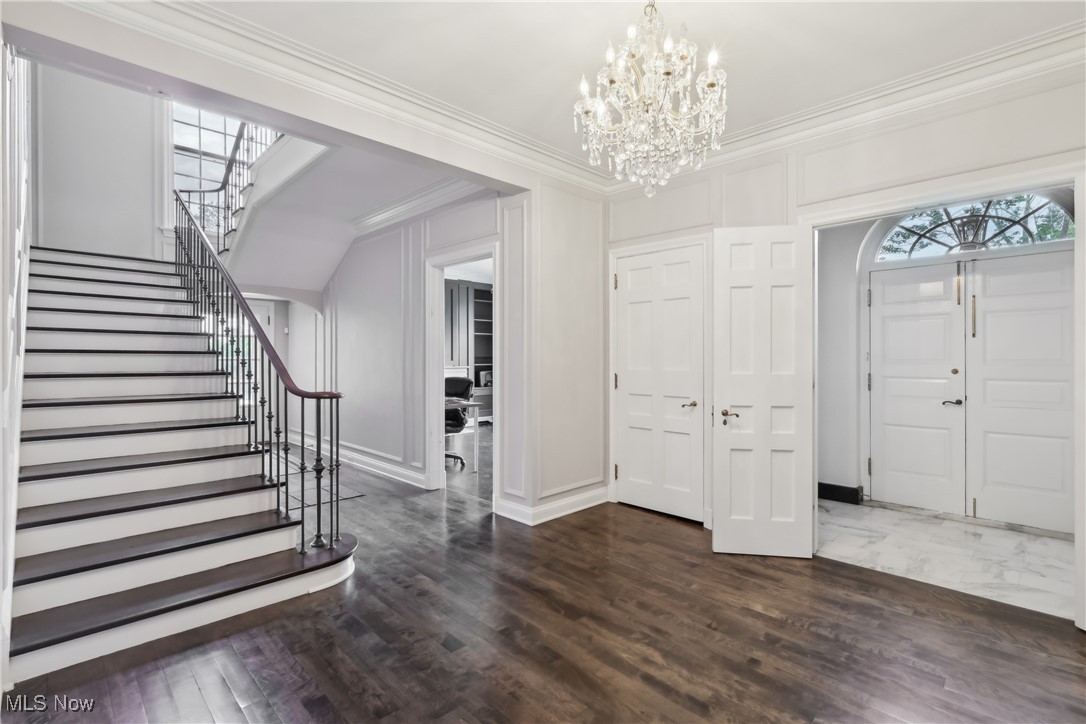Entrance foyer with crown molding, a chandelier, stairway, baseboards, and dark wood-style flooring