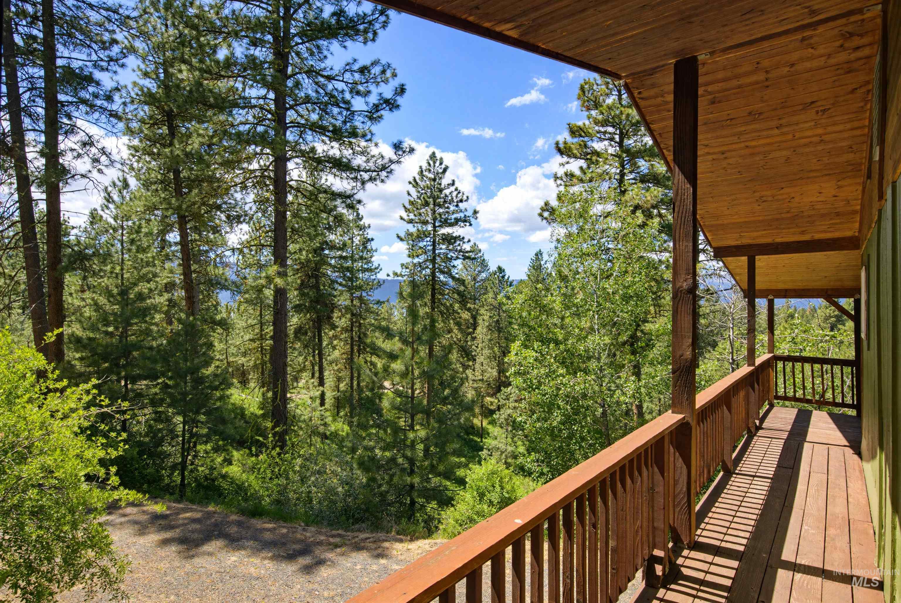 79 Sunset Loop Cascade, ID 83611 - Photo 38 of 44 Wood-finish deck with a rustic railing and exposed beam ceiling, offering expansive views of mature evergreen trees and distant natural scenery