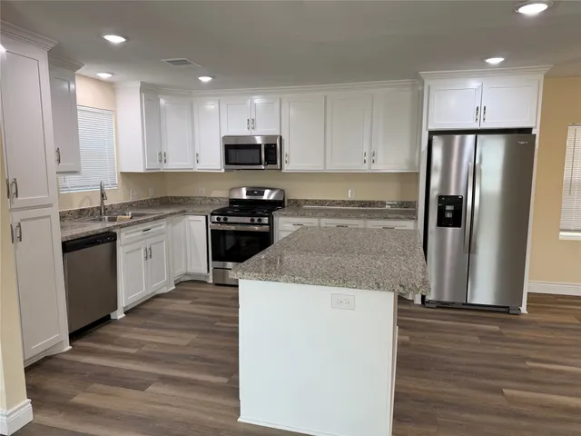 a kitchen with stainless steel appliances granite countertop a refrigerator a stove top oven a sink and dishwasher with wooden floor