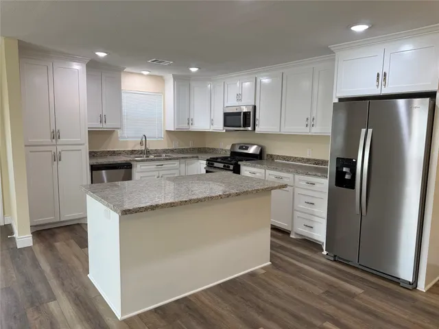 a kitchen with stainless steel appliances granite countertop a refrigerator a stove a sink and white cabinets with wooden floor