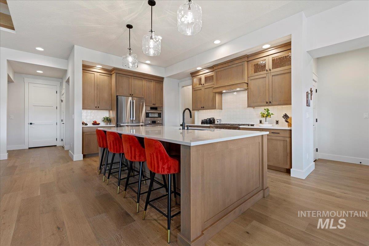 280 North Boulder Rdg Way Eagle, ID 83616 - Photo 13 of 50 Kitchen featuring a breakfast bar area, glass insert cabinets, stainless steel appliances, a large island with sink, and hanging light fixtures