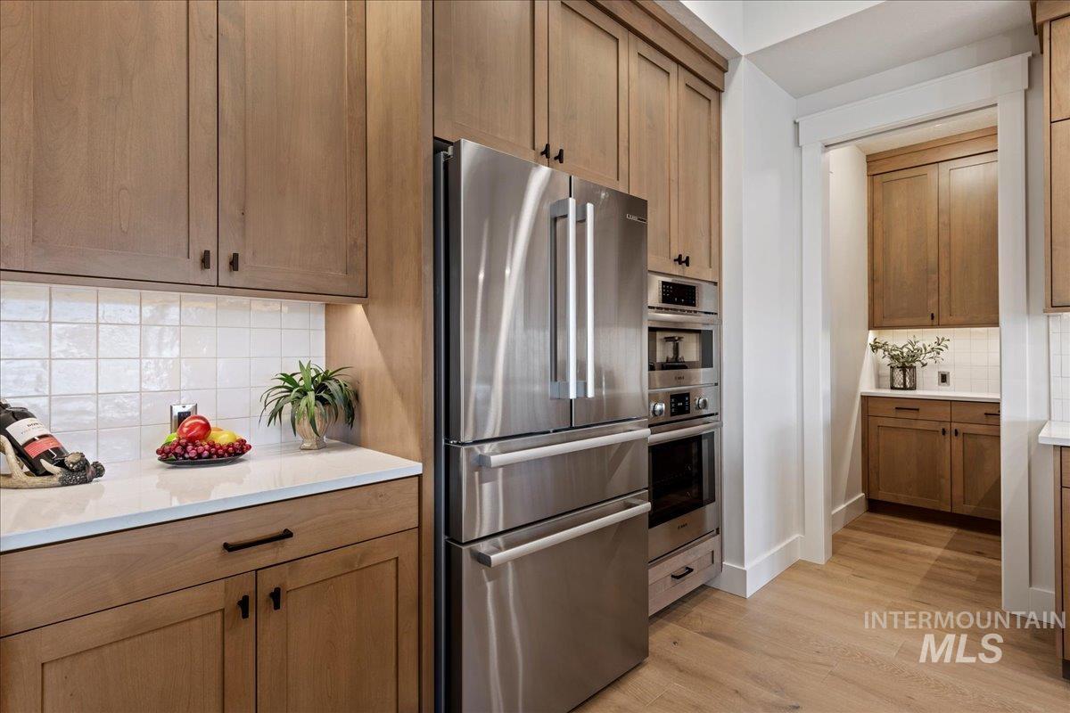 280 North Boulder Rdg Way Eagle, ID 83616 - Photo 15 of 50 Kitchen with decorative backsplash, stainless steel appliances, light wood-type flooring, and brown cabinetry