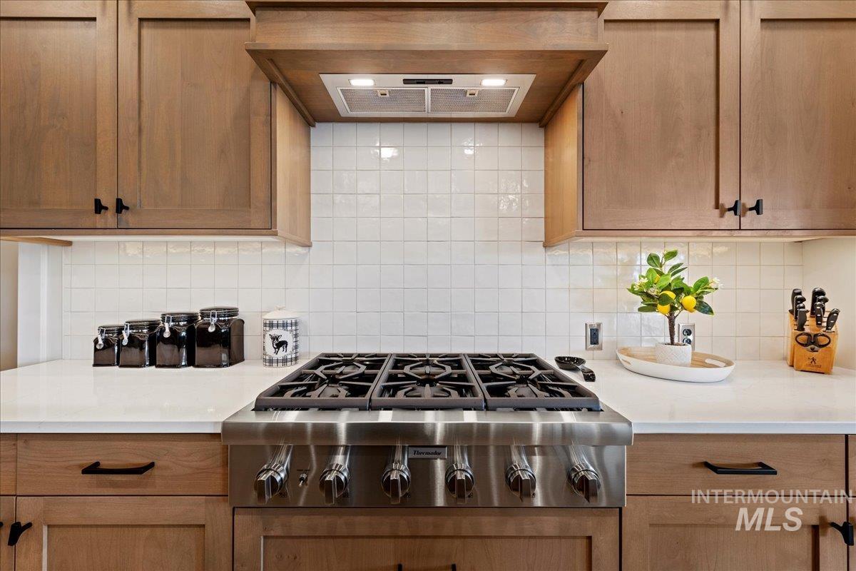 280 North Boulder Rdg Way Eagle, ID 83616 - Photo 16 of 50 Kitchen featuring stainless steel gas cooktop, exhaust hood, decorative backsplash, and light stone counters