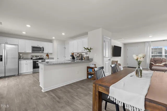 a kitchen with stainless steel appliances kitchen island granite countertop a refrigerator a stove a sink a dining table and chairs with wooden floor