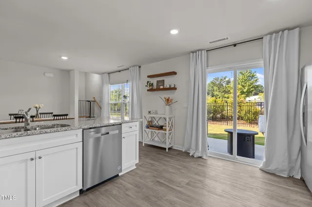 a kitchen with a stove a sink and white cabinets with wooden floor next to windows
