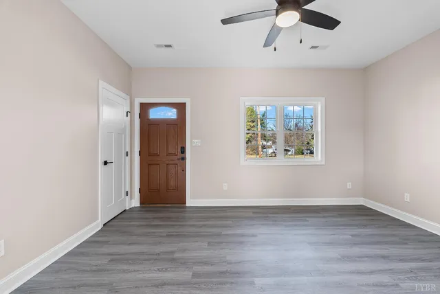 an empty room with wooden floor ceiling fan and windows