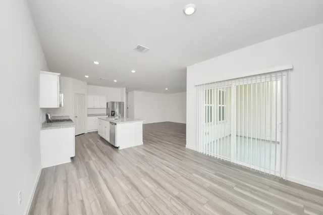 a large white kitchen with kitchen island a stove a refrigerator wooden floor and white walls