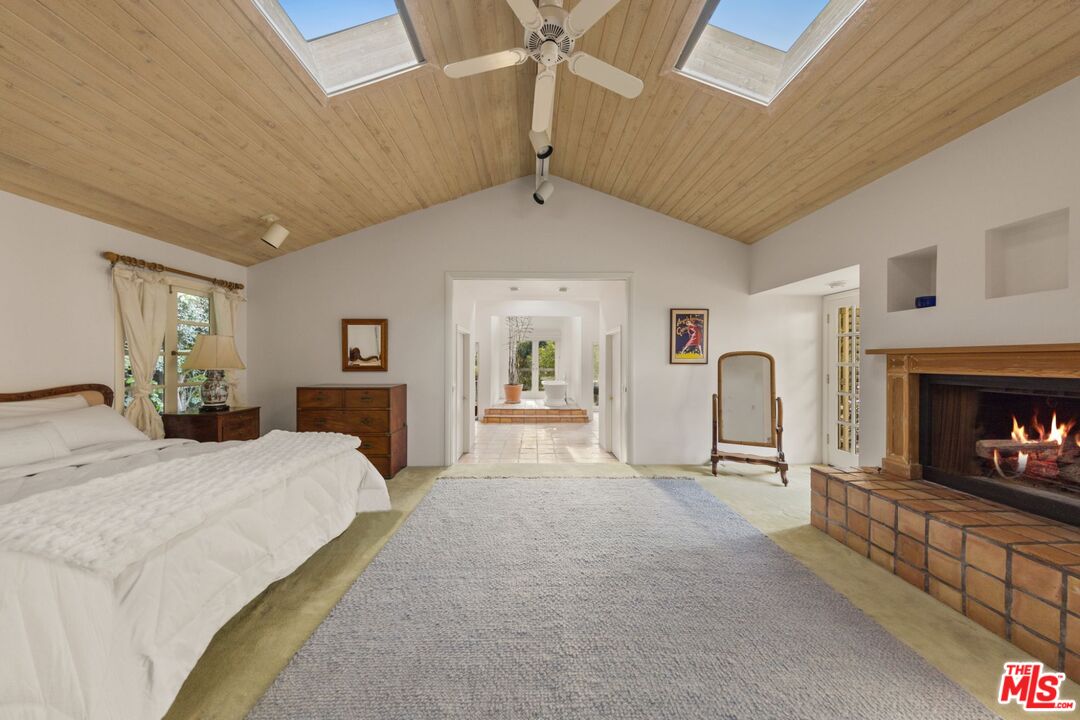 635 North Bonhill Road Los Angeles, CA 90049 - Photo 9 of 19 a spacious bedroom with a bed a fireplace and a large mirror