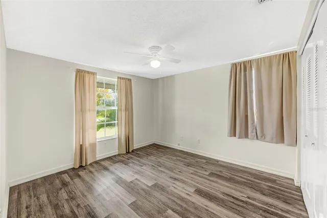 an empty room with wooden floor fan and windows