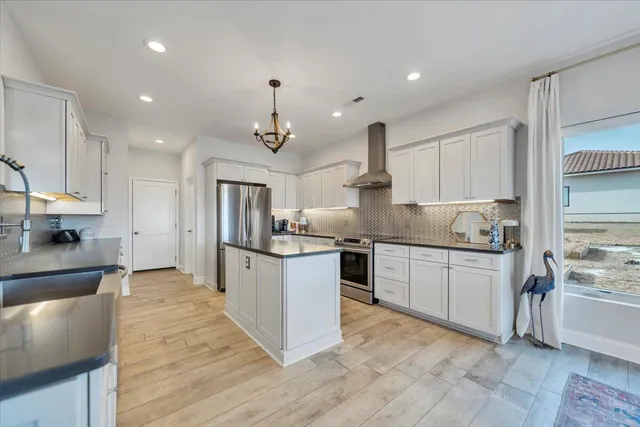 a kitchen with stainless steel appliances granite countertop a refrigerator a sink dishwasher a stove and white cabinets with wooden floor