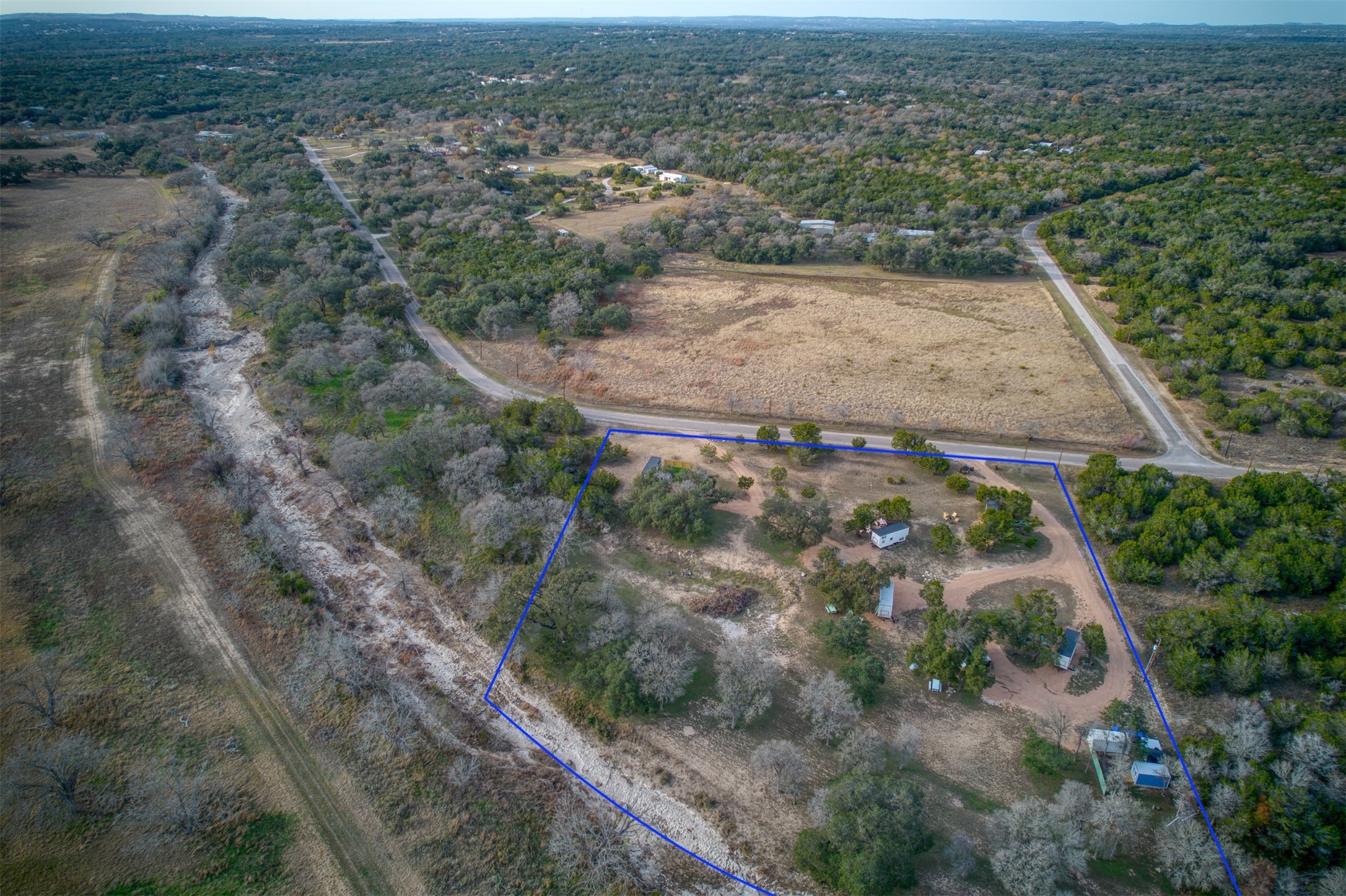 1156 Narrows Road Blanco, TX 78606 - Photo 20 of 40 Expansive aerial view of a property featuring multiple structures, mature trees, and a dirt pathway