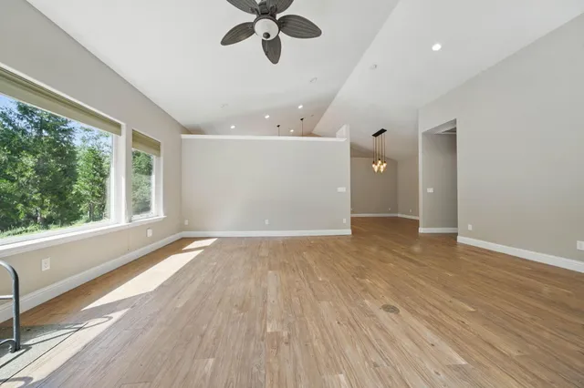an empty room with wooden floor fan and windows