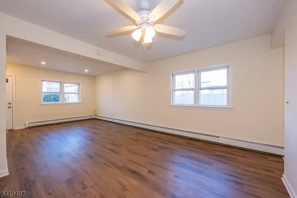 an empty room with wooden floor chandelier fan and windows