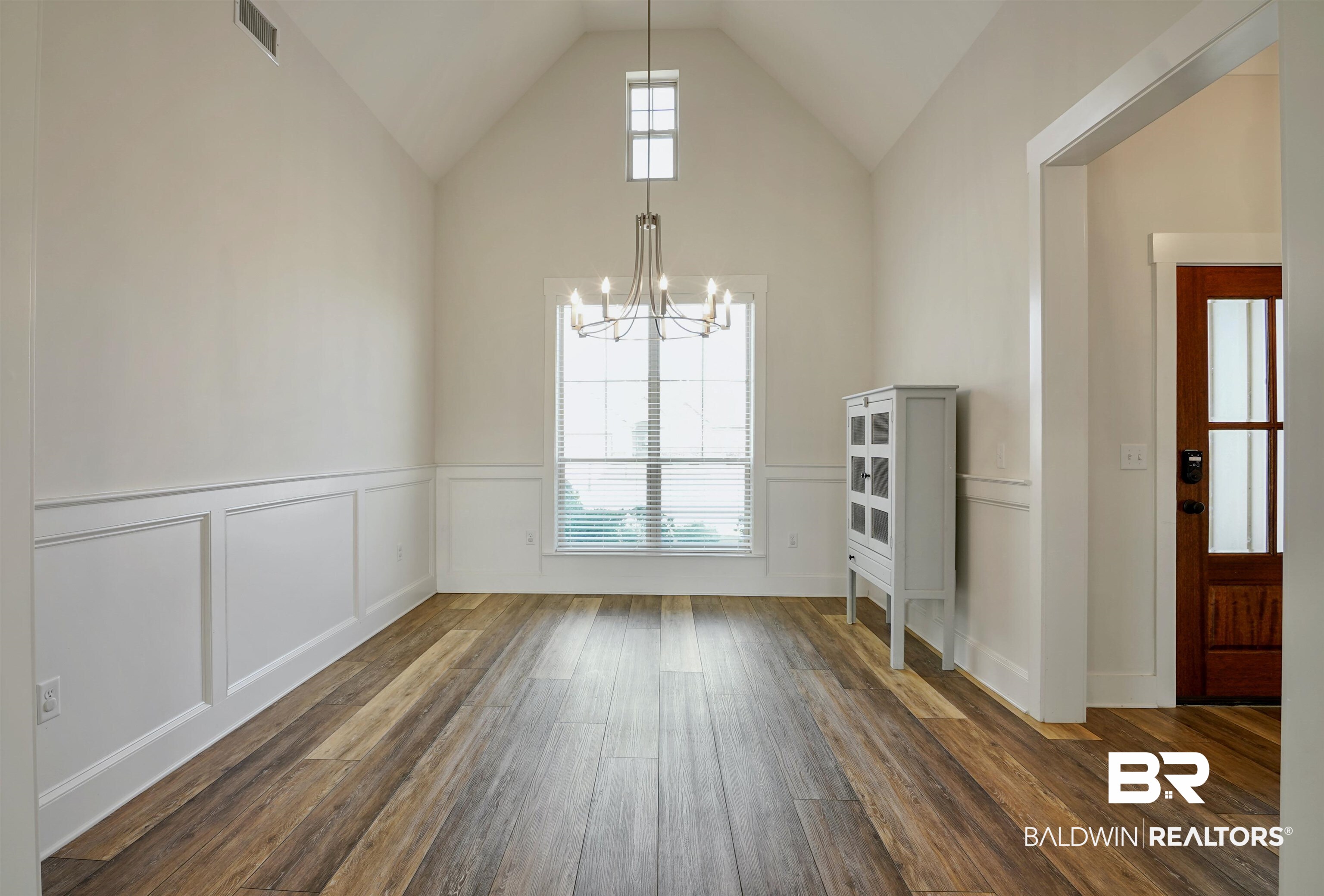 7090 Rocky Rd Loop Gulf Shores, AL 36542 - Photo 4 of 34 Unfurnished dining area with a decorative wall, a wainscoted wall, visible vents, vaulted ceiling, and dark wood finished floors