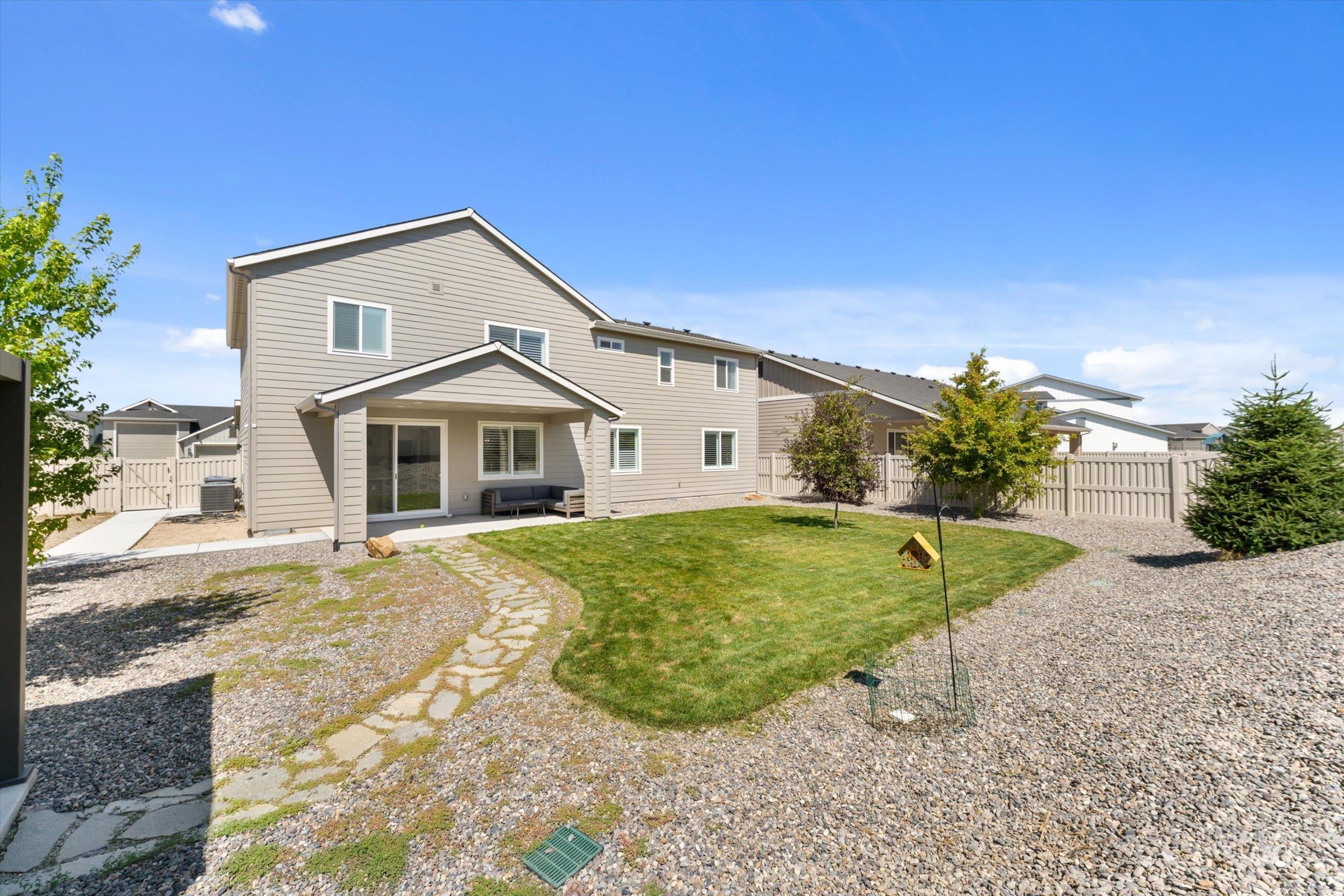 2172 Savoy Court Middleton, ID 83644 - Photo 31 of 46 Rear exterior featuring a covered patio with direct access via sliding glass doors, a stone pathway, a manicured lawn, and natural wood fencing