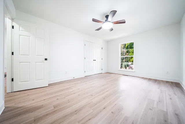 an empty room with wooden floor fan and windows