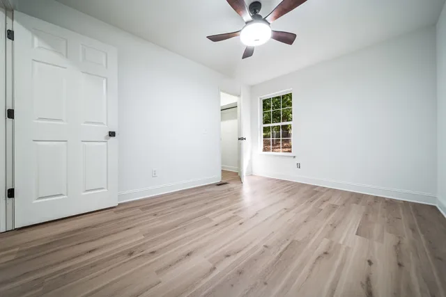 an empty room with wooden floor chandelier fan and windows