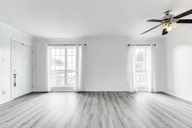 an empty room with wooden floor fan and windows