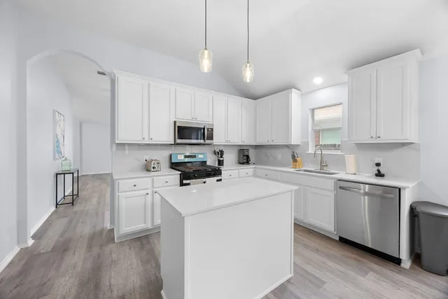 a kitchen with stainless steel appliances granite countertop a sink a stove a refrigerator cabinets and a wooden floor