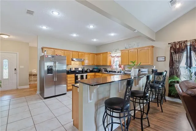 a kitchen with granite countertop a refrigerator a stove a sink a dining table and chairs with wooden floor