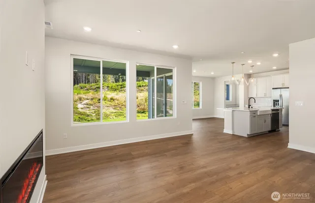 a view of an empty room with wooden floor and a kitchen