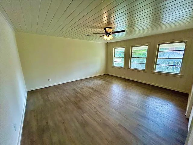 an empty room with wooden floor fan and windows