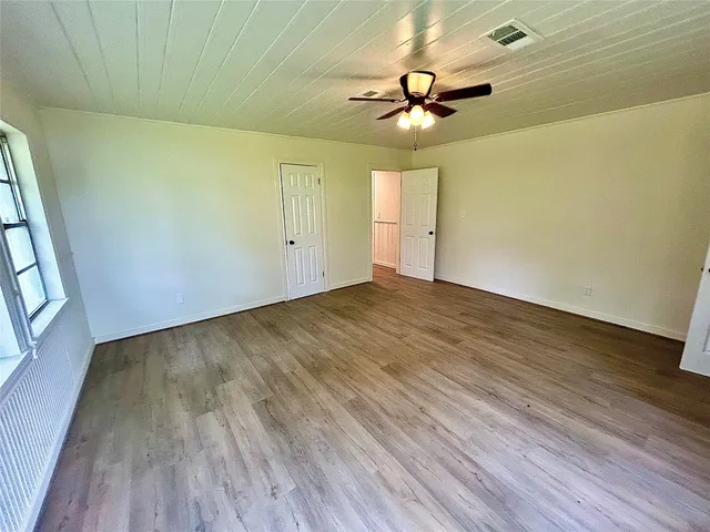 a view of an empty room with wooden floor and a ceiling fan