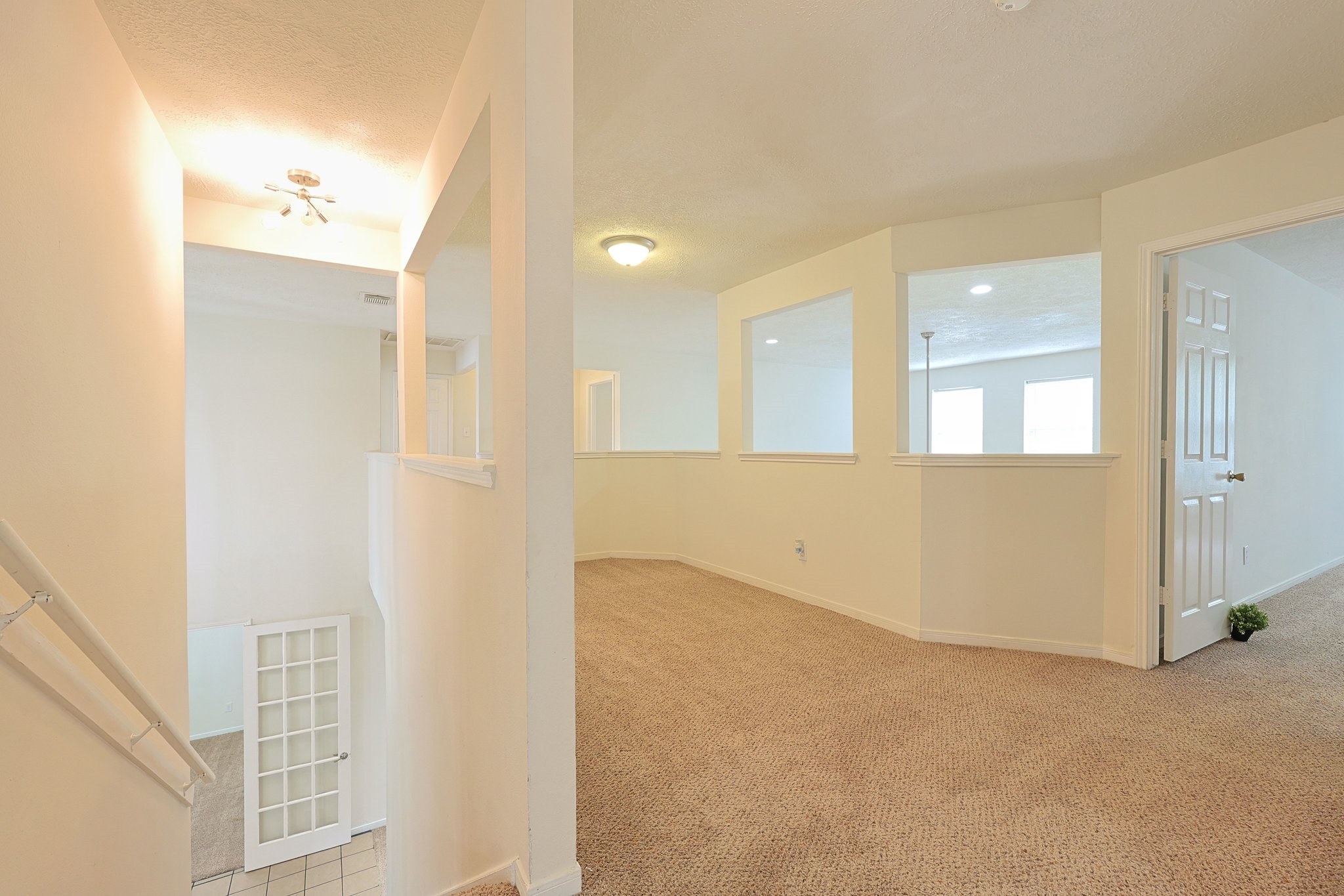 23019 Eastgate Village Drive Spring, TX 77373 - Photo 34 of 46 This photo shows a bright, spacious upstairs area with carpeted floors, neutral walls, and multiple open doorways leading to other rooms. A stairway with a white railing descends to the lower level, and a door with glass panels adds elegance. The area is well-lit with natural and ceiling lights, creating an inviting space.