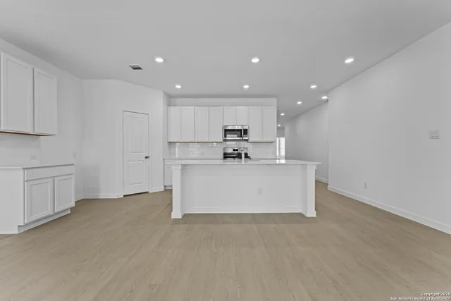 a view of kitchen with kitchen island stainless steel appliances sink refrigerator and white cabinets