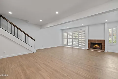 a view of an empty room with wooden floor fireplace and a window