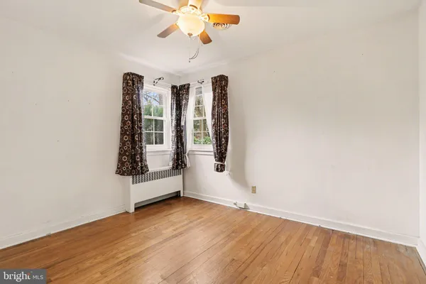 an empty room with wooden floor chandelier fan and windows