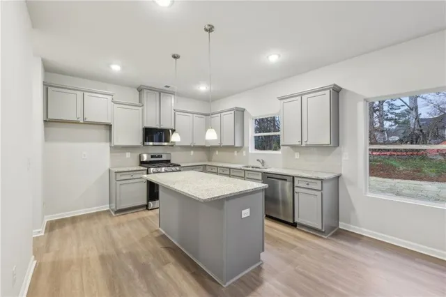 a kitchen with stainless steel appliances granite countertop a stove top oven a sink dishwasher a refrigerator and white cabinets with wooden floor