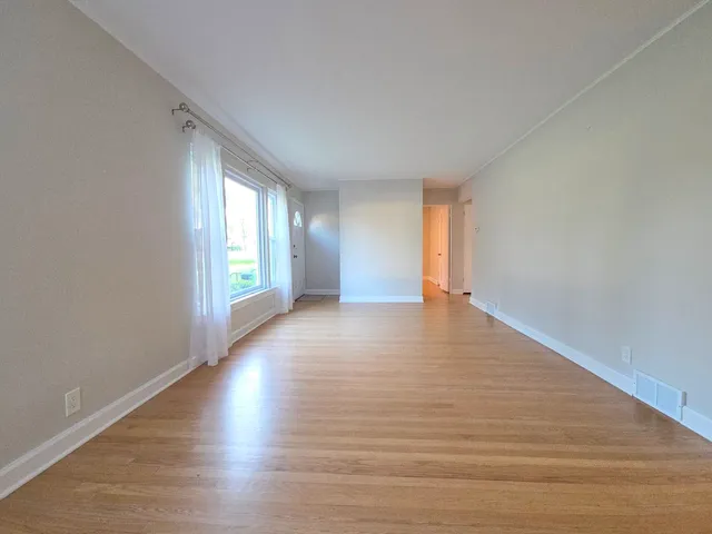 a view of an empty room with wooden floor and window