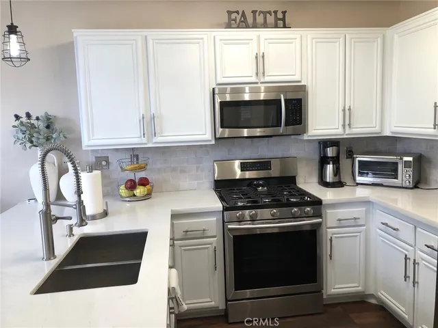 a kitchen with stainless steel appliances granite countertop white cabinets a stove a microwave and a sink