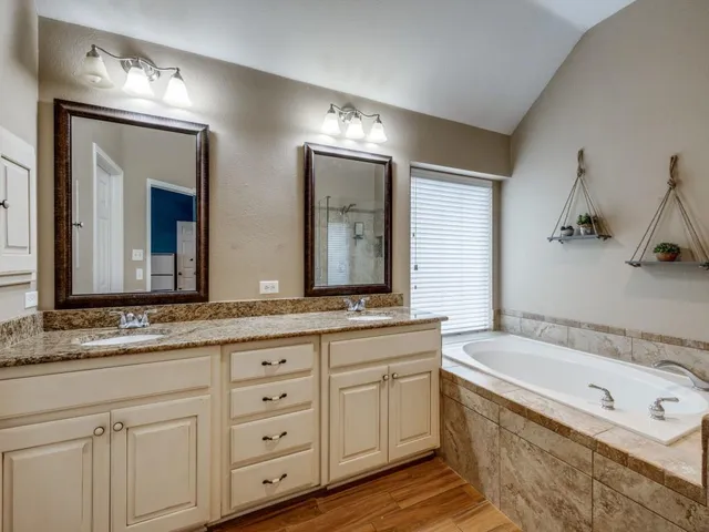 a bathroom with a granite countertop double vanity sink a mirror and a bathtub