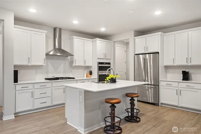 a kitchen with stainless steel appliances a stove a sink a refrigerator white cabinets and wooden floor