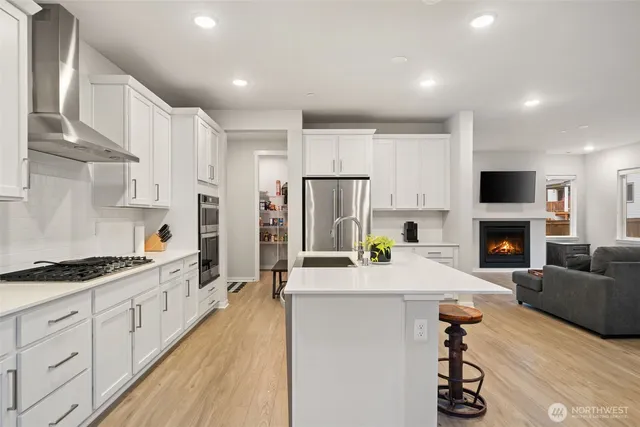a kitchen with stainless steel appliances kitchen island granite countertop a refrigerator a stove a sink dishwasher and a fireplace with wooden floor