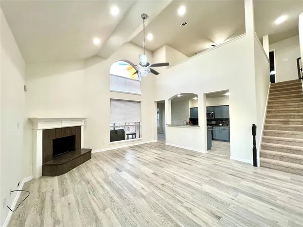 a view of an empty room and kitchen with fireplace wooden floor
