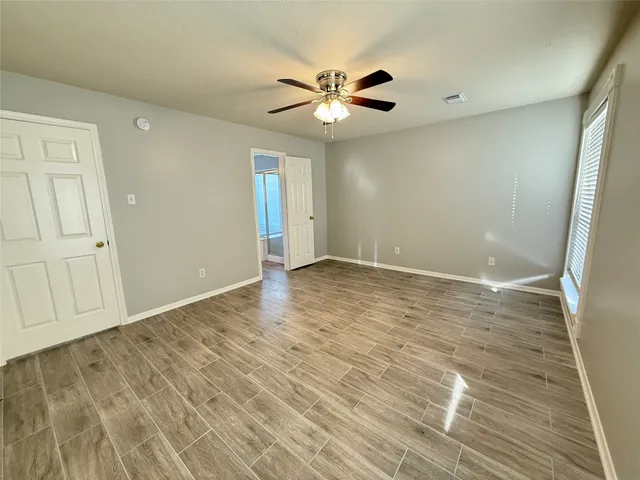 a view of an empty room with wooden floor and a ceiling fan