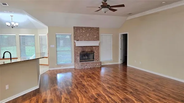 an empty room with wooden floor a ceiling fan a fireplace and windows