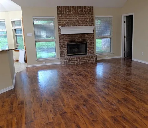 an empty room with wooden floor fireplace and windows