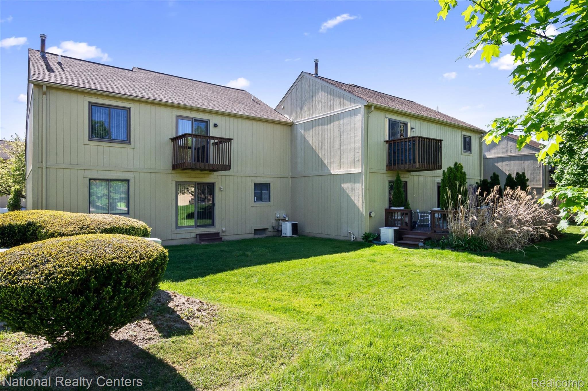 2203 Rochelle Park Drive Rochester, MI 48309 - Photo 42 of 43 Rear exterior featuring two levels of living space, individual balconies, a ground-level patio, and a manicured lawn