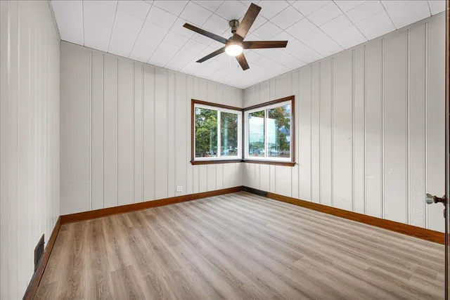 an empty room with wooden floor chandelier fan and windows